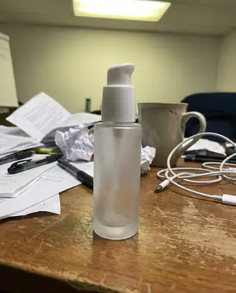 Concept: an unbranded pump bottle shot flat on a cluttered desk, before art direction